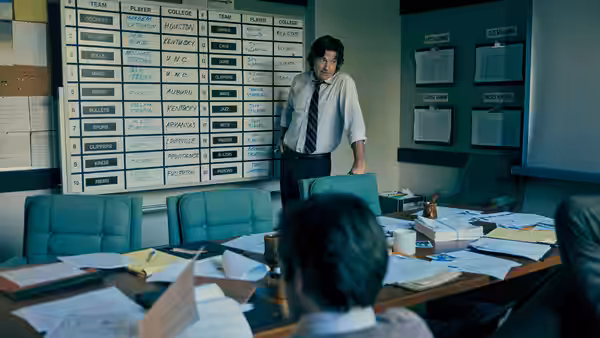 Man in tie standing before wall of player statistics charts