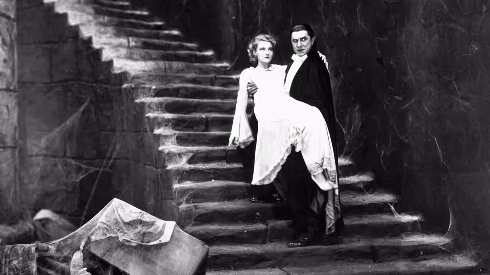 Count Dracula (Bela Lugosi) carries a woman in a white dress down a stone staircase