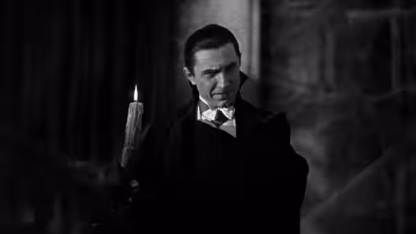 Count Dracula (Bela Lugosi) stands beside a lit candle in a dark room