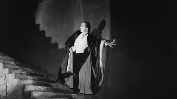 Count Dracula (Bela Lugosi) spreads his arms beside a staircase