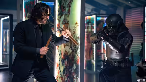 John Wick (Keanu Reeves) aiming a pistol while holding a shotgun