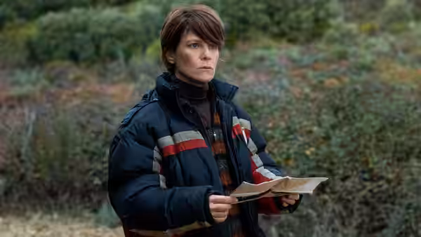 A woman holds papers while standing amid green bushes outdoors
