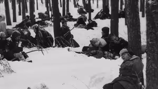 Armed partisans lie and crouch among snow-covered trees in a forest