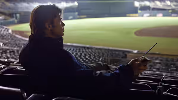 Billy Beane (Brad Pitt) sits in empty stadium seats holding a device