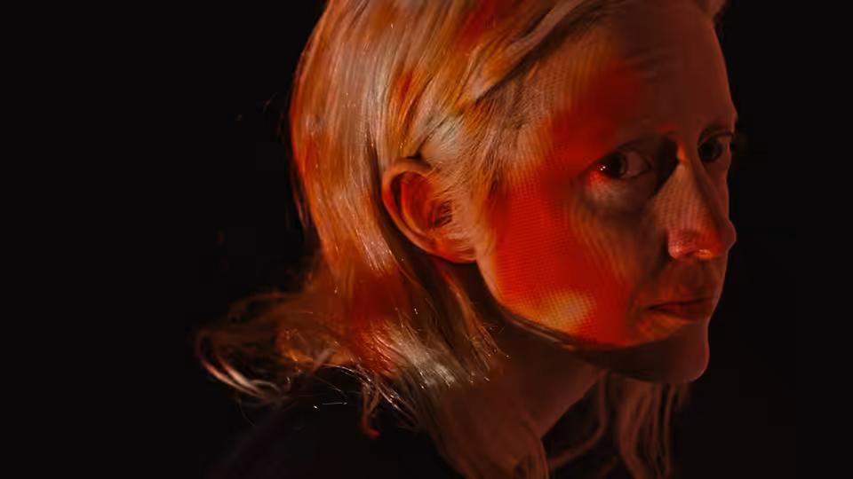 A blonde woman turns toward the light in a dark room