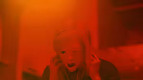 A blonde woman holds her hands to her ears beneath red light
