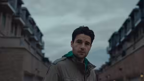 Colin Tate (Christopher Abbott) stands between rows of houses beneath an overcast sky