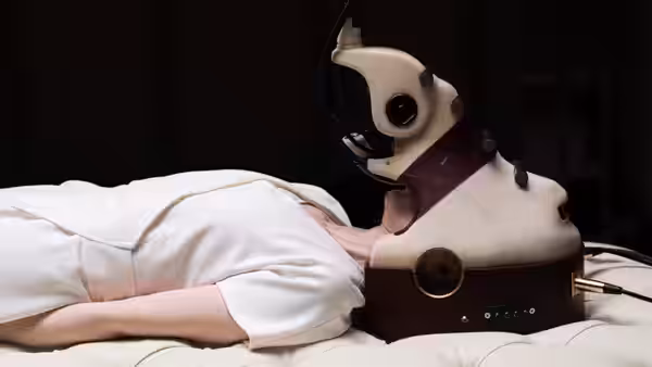 A person lies beneath a bulky white headset connected to laboratory equipment
