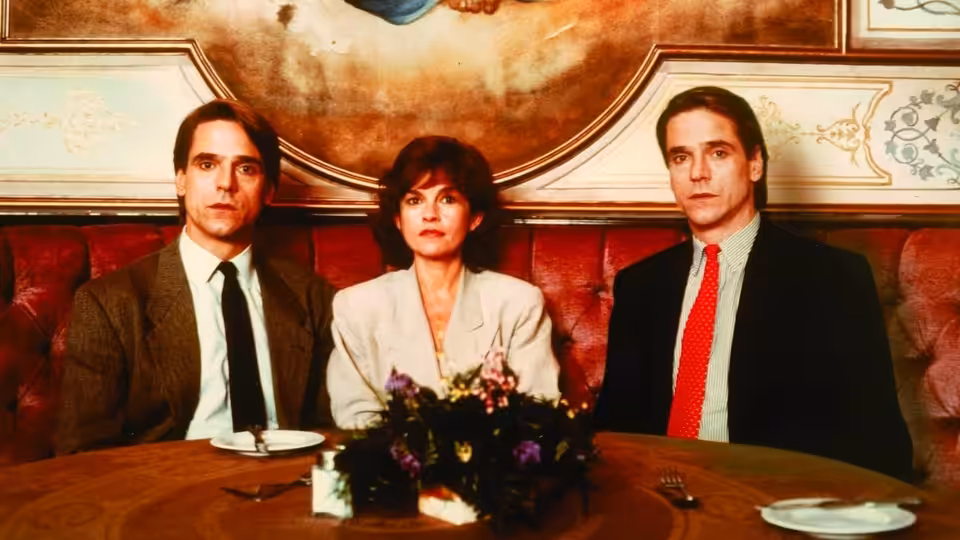 Twin brothers in suits sit with a woman at a restaurant table