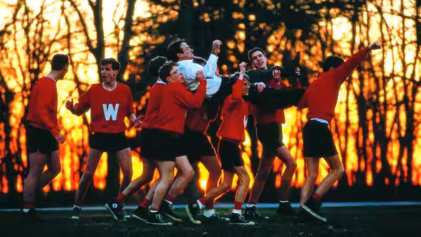 Boys in red uniforms carrying a teammate on their shoulders outdoors
