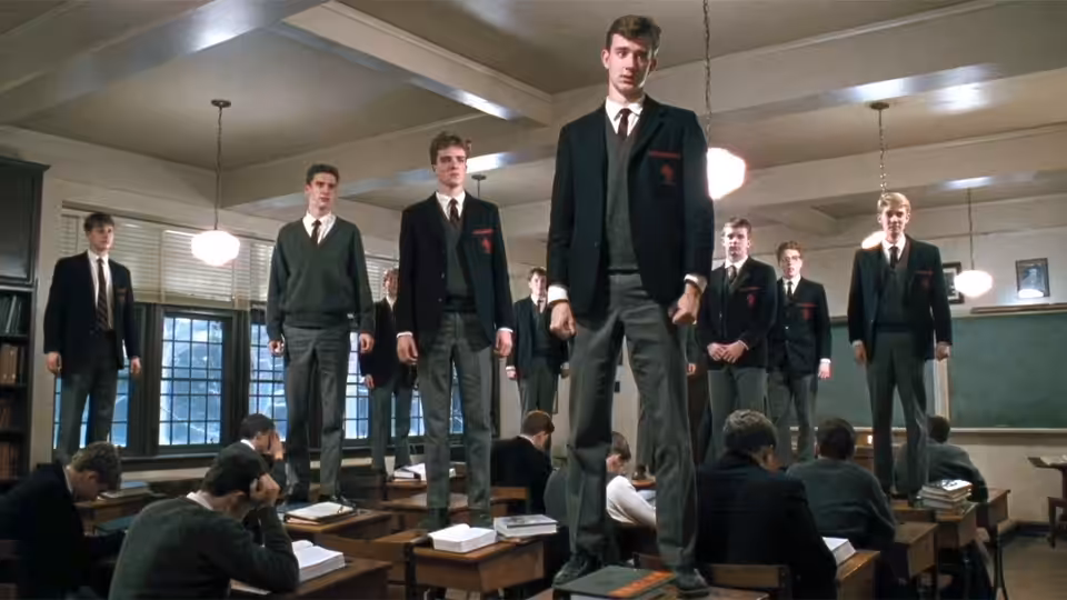 Students in school uniforms standing on desks inside a classroom