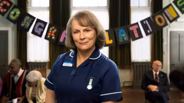 Sister Gilpin (Jennifer Saunders) smiles in front of congratulations banner