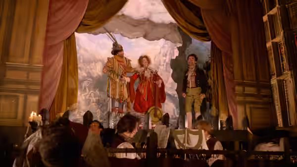 A man and woman stand onstage before a painted backdrop as spectators watch