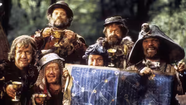 A group of bearded travelers holds up a map in the woods
