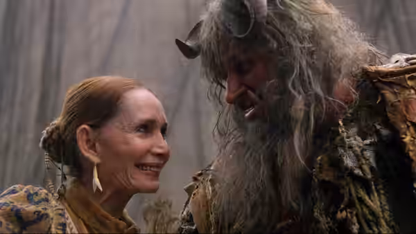 A smiling woman faces a horned, shaggy-haired man in the forest