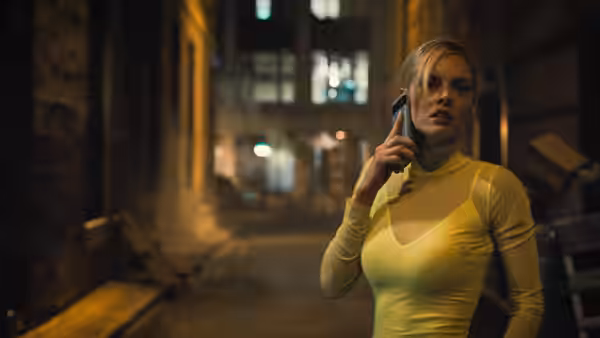 a woman in a yellow top talking on a phone in a dimly lit alley
