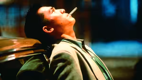 Chow Yun-Fat resting against a car with a cigarette in his mouth