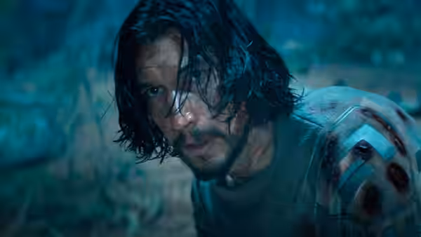 Mills (Adam Driver) with wet hair and injuries looks ahead in a forest