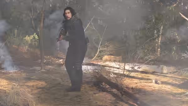 Mills (Adam Driver) stands in a smoky forest holding a weapon