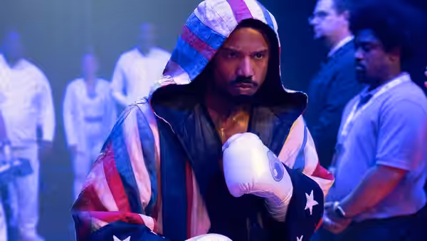 Damian Dame Anderson (Jonathan Majors) in a flag hoodie with gloves