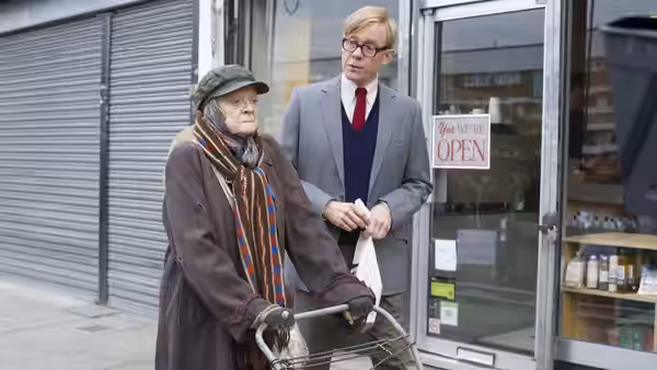 Alan Bennett (Alex Jennings) stands beside Miss Shepherd (Maggie Smith) and her wheeled cart outside a shop