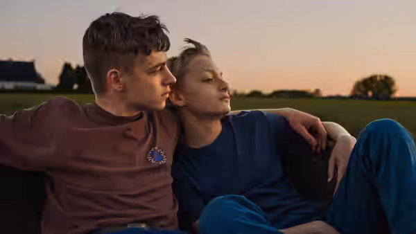 Léo (Eden Dambrine) and Rémi (Gustav De Waele) sitting together at dusk outdoors