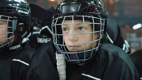 Rémi (Gustav De Waele) in hockey gear seated on the bench