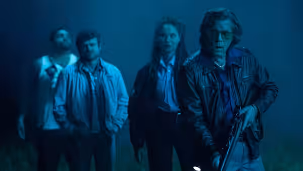 Four people standing in a dark misty area with one holding a shotgun