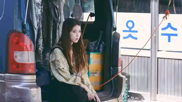 So-young (IU) sitting beside an open van on a street