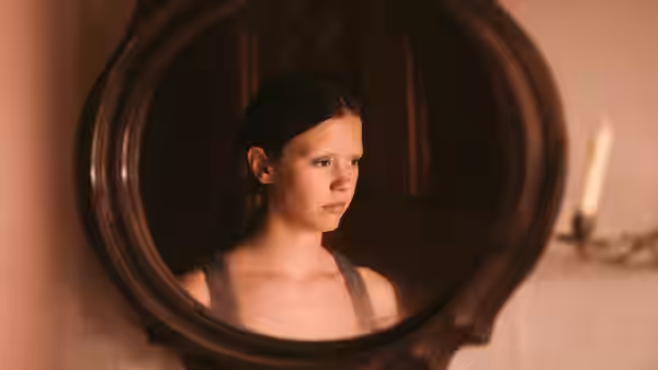 A young woman with wet hair looks aside in a round mirror reflection