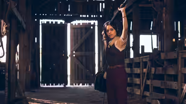 A woman stands inside a wooden barn holding a strap overhead