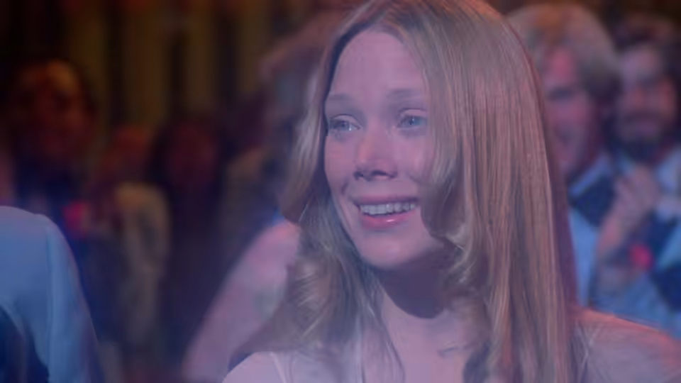 Carrie (Sissy Spacek) smiling at the prom with an audience behind her