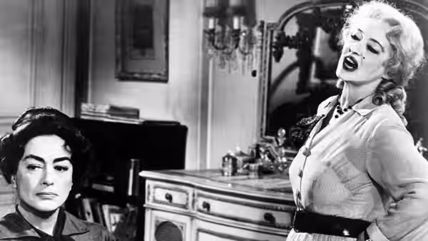 Blanche Hudson (Joan Crawford) sits as Baby Jane Hudson (Bette Davis) poses in the kitchen
