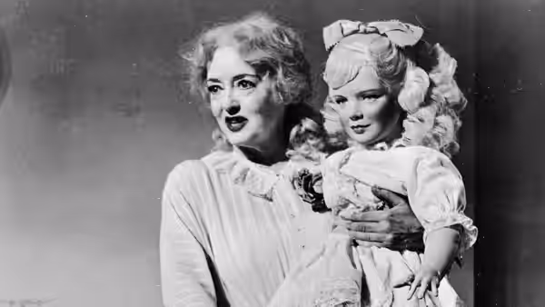 Baby Jane Hudson (Bette Davis) holds a little girl dressed in a ruffled costume