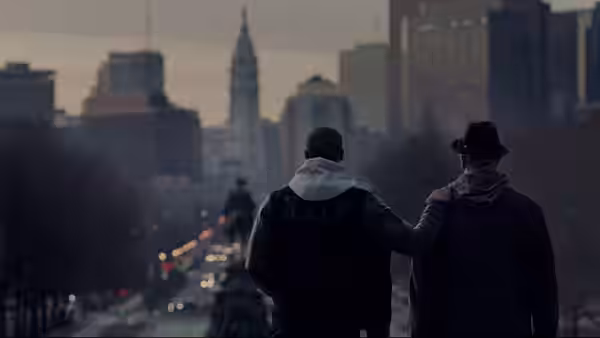 Two men standing with arms around each other overlooking a city skyline