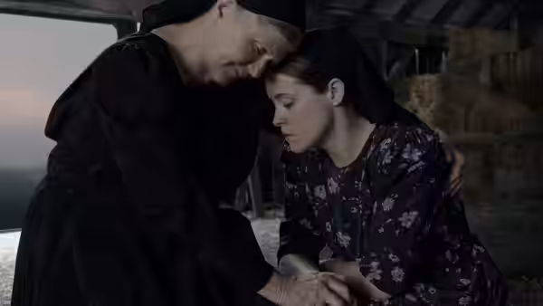 an older woman comforting another while seated in a barn