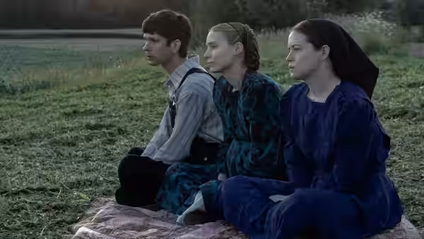 a man and two women seated on a blanket in a grassy field