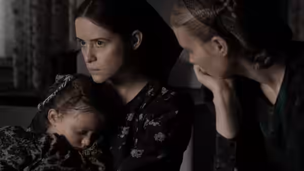 two women looking at a sleeping child resting against them