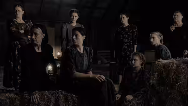 women gathered on hay bales inside a dimly lit wooden barn