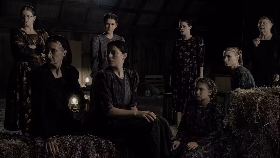 women gathered on hay bales inside a dimly lit wooden barn