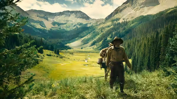 a bearded man walking through a lush mountain valley