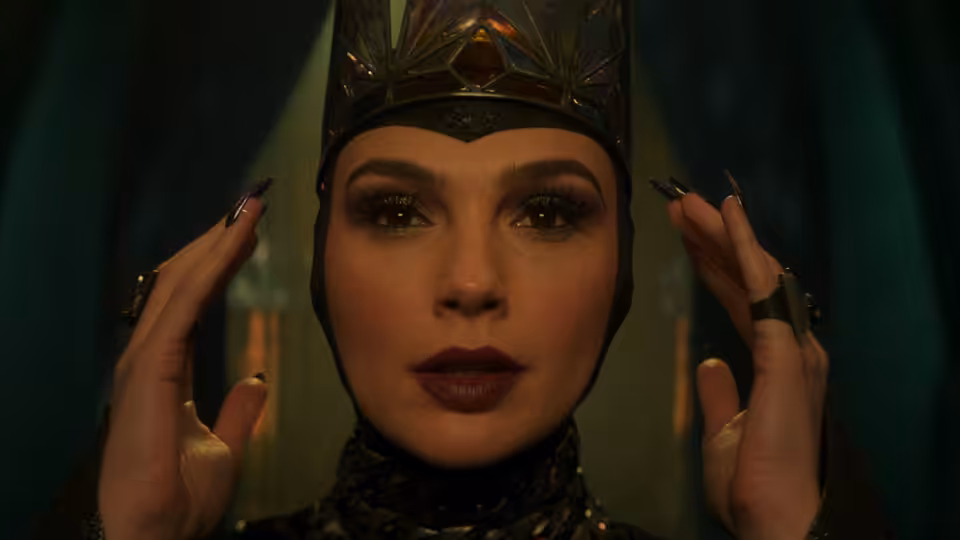 Gal Gadot as the Evil Queen raises her hands beside her face with long nails