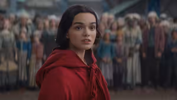 Rachel Zegler as Snow White in a red cloak glances back at a crowd