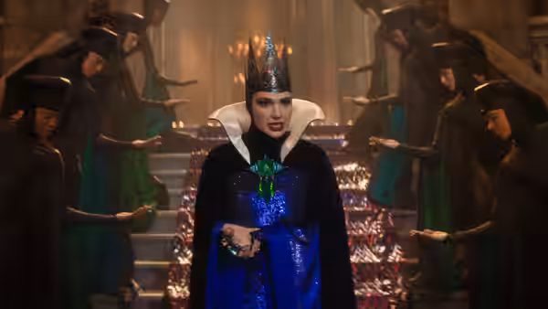 Gal Gadot as the Evil Queen stands in a torchlit hall with attendants in dark robes