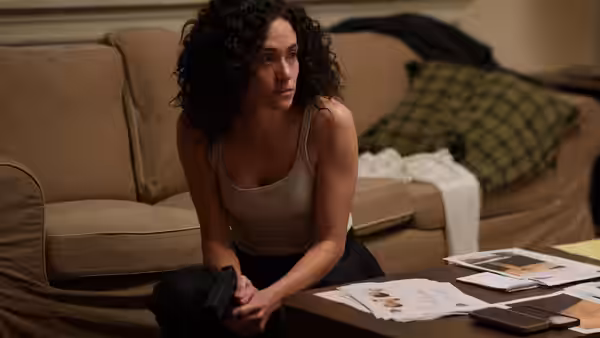Alice Black (Emmy Rossum) kneels on the floor before a table of photographs