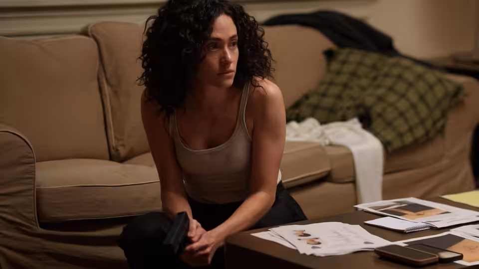 Alice Black (Emmy Rossum) kneels on the floor before a table of photographs