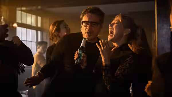 A man with glasses holds a beer bottle while a woman cheers at a party