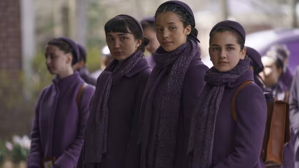three young women in purple coats and scarves stand outdoors together