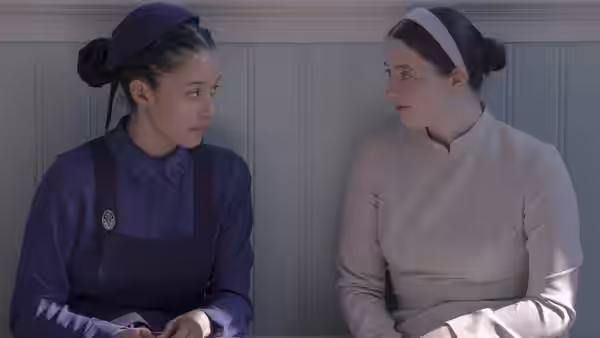 two women in head coverings sit facing each other indoors