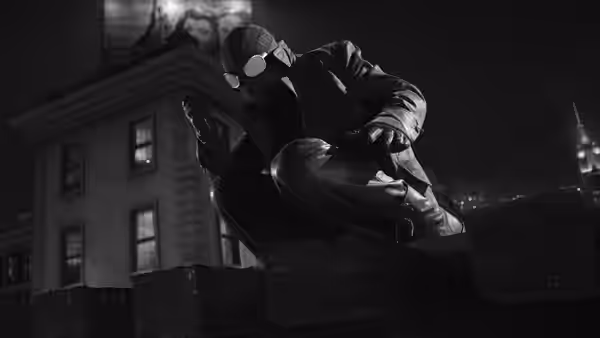 A masked man in a beanie crouching on a building ledge at night